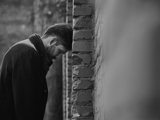 Frustrated depressed young man near the brick wall looking angry. Closeup sad toned dramatic...