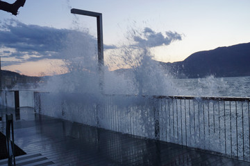 Wave crashing on the pier on lake Maggiore, Ticino on a windy cold spring day at sunset