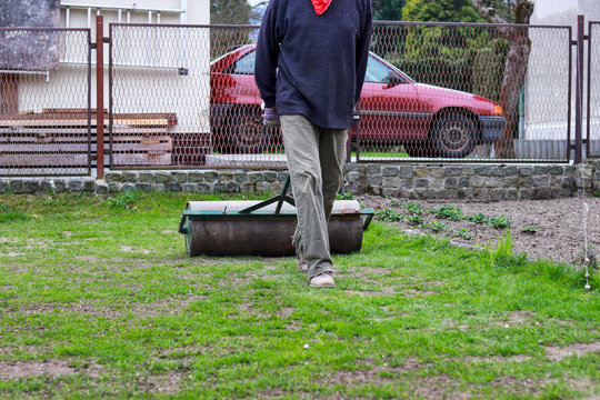 Adult male landscaping garden after long winter. Spring work. Flattening grass surface in the garden. Hard and strenuous garden work. Preparing for plant grass seeds