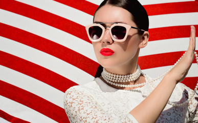 Portrait of a pretty young woman in white lace dess, white pearl necklace and  sunglasses with neon red painted lips