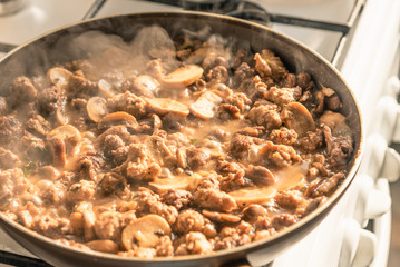 Cooking a stew of homemade sausages and mushrooms in a pan - traditional Italian mushroom sauce Boscaiola.