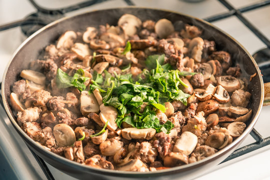 Cooking a stew of homemade sausages and mushrooms in a pan - traditional Italian mushroom sauce Boscaiola.