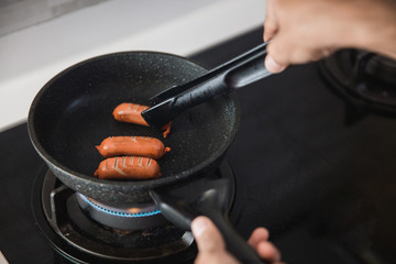 Close up cooking hands using food tongs to frying sausages on a pan