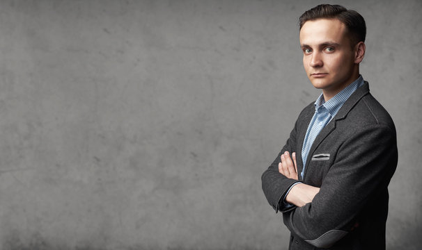 Portrait of young trendy man is standing before gray studio wall