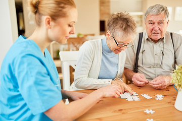 Pflegekraft und Senioren Paar beim Puzzle spielen