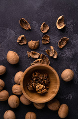 Cracked walnuts in wooden bowl and on black slate surface. Healthy nuts and seeds composition.