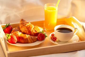 Breakfast in bed, a tray of coffee, croissants, juice and fresh strawberries. Early morning. 