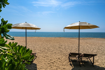 Tropical beach with sun umbrella under the palm trees in sunlight, vacation background