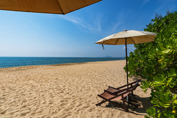 Tropical beach with sun umbrella under the palm trees in sunlight, vacation background