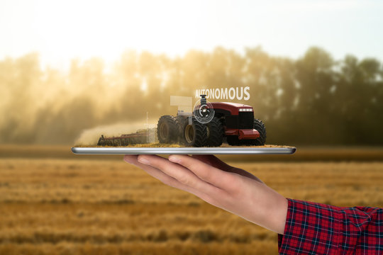 Farmer holding a tablet with autonomous tractor. Smart farming