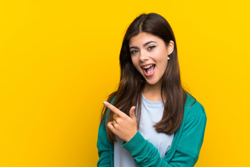 Teenager girl over yellow wall pointing finger to the side