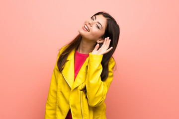 Teenager girl over pink wall listening to something by putting hand on the ear