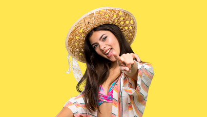 Teenager girl on summer vacation points finger at you while smiling over isolated yellow background