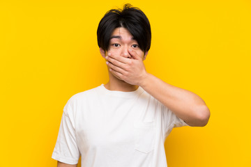 Asian man over isolated yellow wall covering mouth with hands