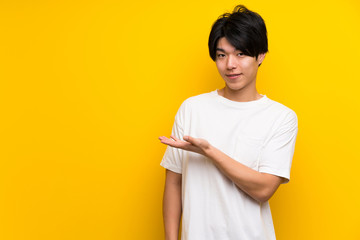 Asian man over isolated yellow wall presenting an idea while looking smiling towards