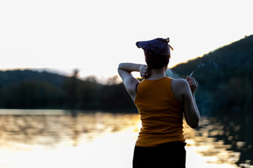 Mujer de espaldas fumando delante del lago al atardecer