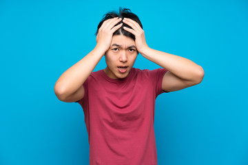 Asian man with red shirt over isolated blue wall with surprise facial expression