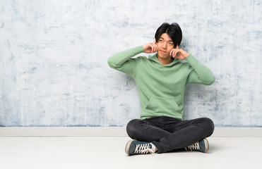 Asian man sitting on the floor having doubts and thinking