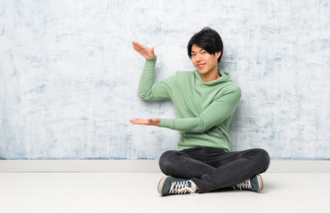Asian man sitting on the floor holding copyspace to insert an ad