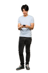 A full-length shot of a Asian man with blue shirt sending a message with the mobile over isolated white background