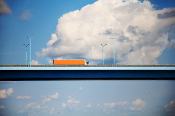 Side view of semi-truck with cargo trailer driving on a high bridge with sky and clouds in the background