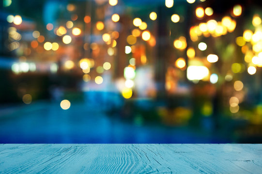 blur light of bar or pub beside blue water swimming pool summer party at night with top of wood table background