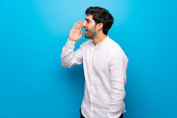 Young man over isolated blue wall shouting with mouth wide open to the lateral
