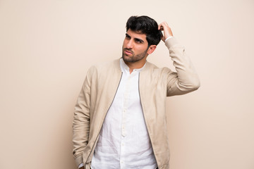 Young man over isolated wall having doubts while scratching head