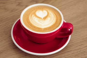 Red cup with cappuccino on a wooden table. 