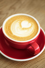 Red cup with cappuccino on a wooden table. 