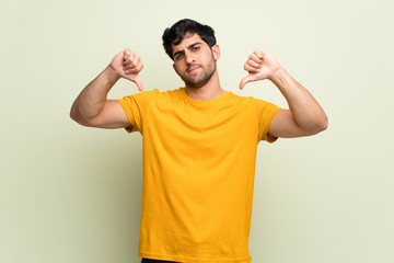 Young man over pink wall showing thumb down with both hands