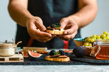 Food recipe concept. Toasts of cheese, figs and honey in hands in the kitchen. This Fig and Gorgonzola tartines, toast, bruschetta. drizzled with honey