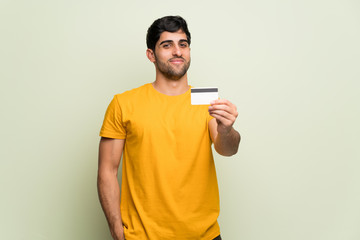 Young man over pink wall holding a credit card