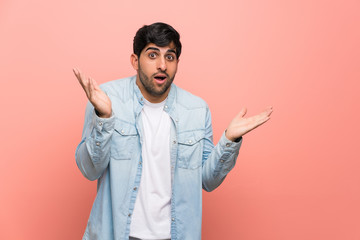 Young man over pink wall with shocked facial expression