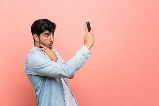 Young man over pink wall making a selfie