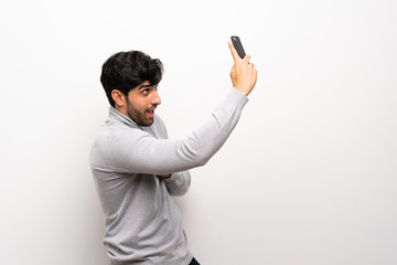 Young man over isolated white wall making a selfie