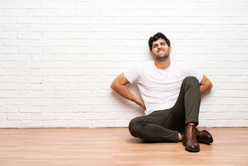 Young man sitting on the floor suffering from backache for having made an effort