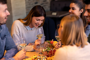 Group of young friends having fun in restaurant, talking and laughing while dining at table.