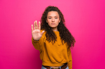 Teenager girl over pink wall making stop gesture