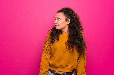 Teenager girl over pink wall making doubts gesture looking side
