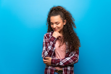 Teenager girl over blue wall looking down with the hand on the chin