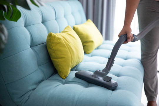 close up of man's hand cleaning couch using vacuum cleaner at home
