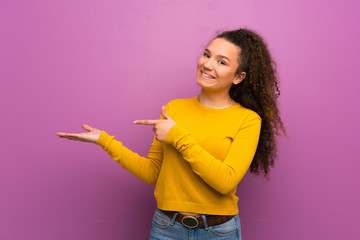 Teenager girl over purple wall holding copyspace imaginary on the palm to insert an ad