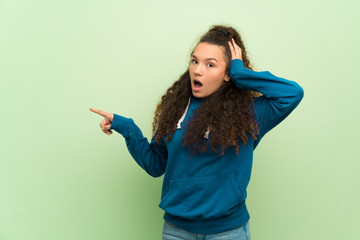 Teenager girl over green wall pointing finger to the side and presenting a product