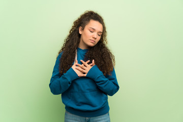 Teenager girl over green wall having a pain in the heart