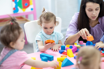 Babies in kindergarten. Kids toddlers in nursery school. Little children preschoolers play with teacher.