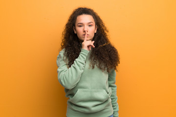 Teenager girl over ocher wall showing a sign of silence gesture putting finger in mouth