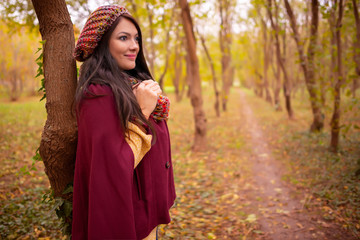 Beautiful girl in stylish autumn fashion clothes, in park scenery with trees and leaves. Gorgeous romantic young woman outdoors. American plan shot in warm natural light, retouched, vibrant colors