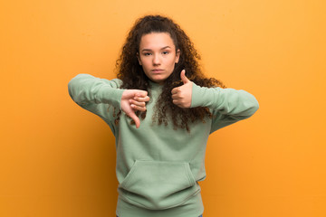 Teenager girl over ocher wall making good-bad sign. Undecided between yes or not