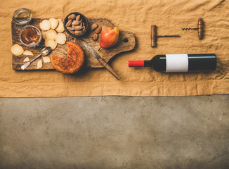 Wine and snack set. Flat-lay of wine bottle with blank label, vintage corkscrews and cheese and appetizers board over dusty yellow linen tablecloth, top view, copy space. Party food concept